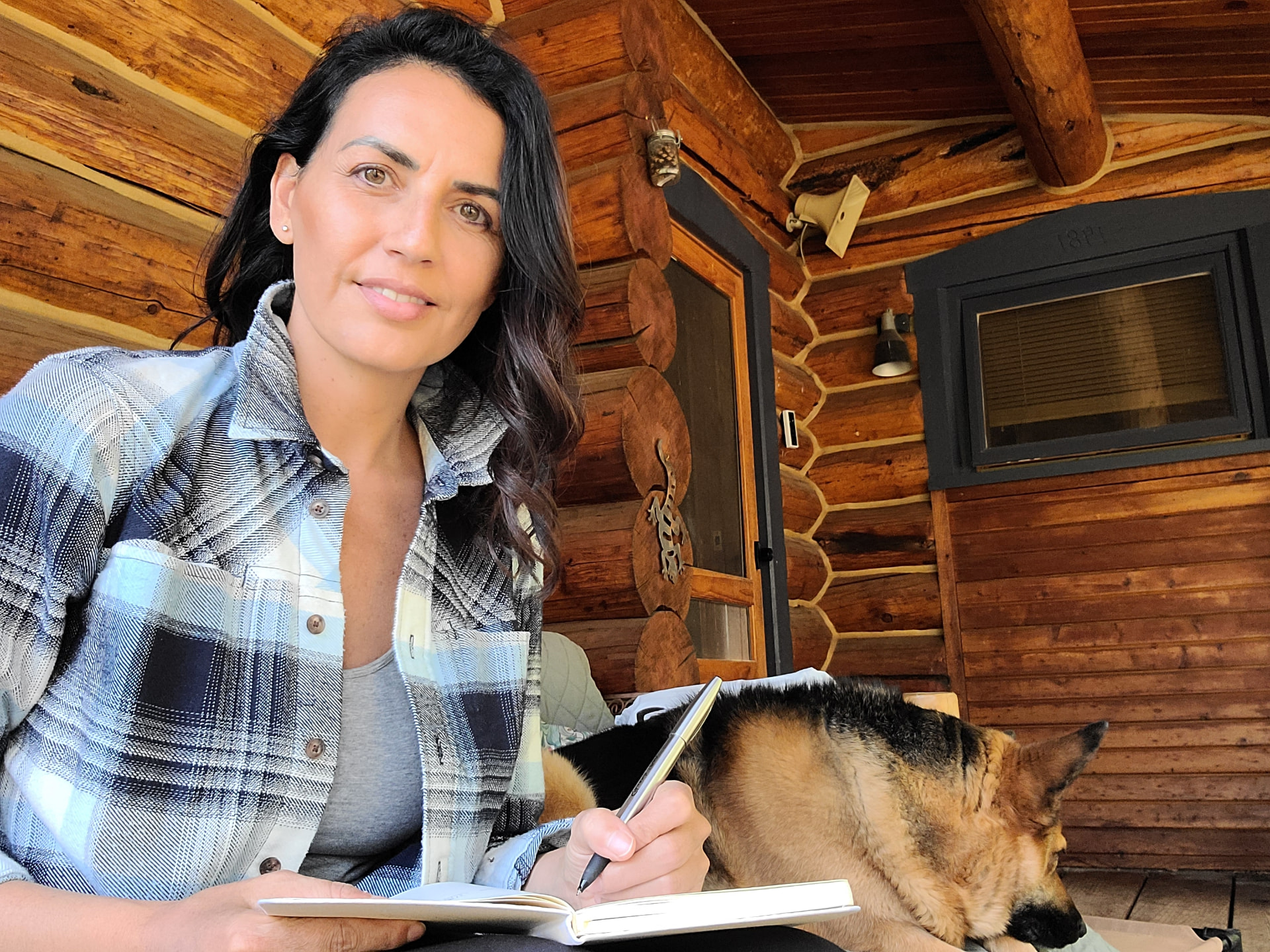 Toni writing in a notebook at a cabin with her dog asleep beside her